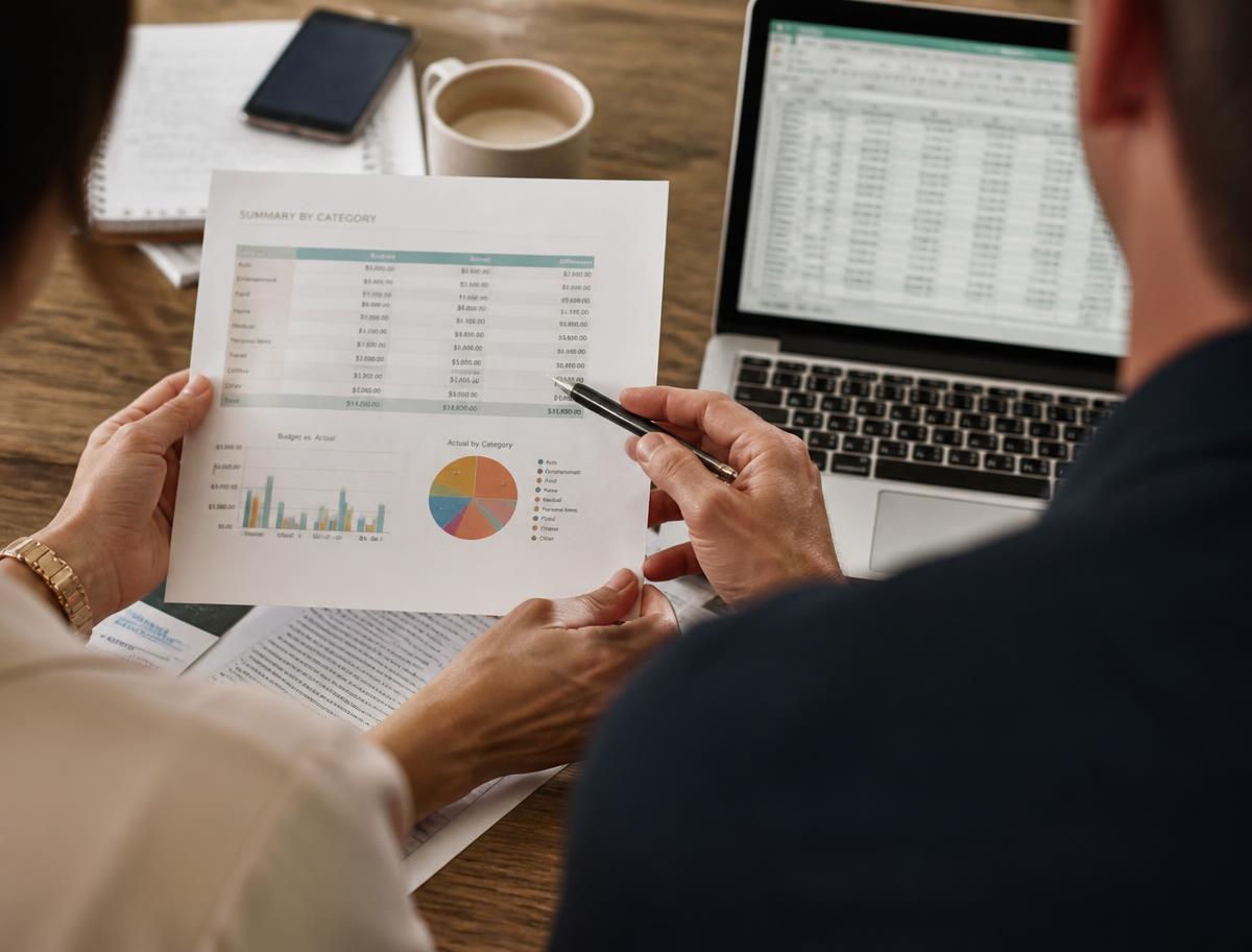 Two people reviewing a printed financial summary alongside a laptop